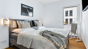 Una camera da letto ordinata con un letto, lampade sui comodini, un quadro incorniciato e una finestra con vista.