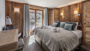 Un dormitorio con pared de madera, una cama con varias almohadas, un escritorio con lámpara y vistas al exterior a través de una puerta de cristal.