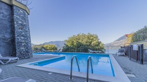 Una piscina con sillas de descanso, un muro de piedra y vistas a montañas.