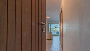 Un pasillo con una puerta de madera, una pared blanca y un suelo de baldosas.