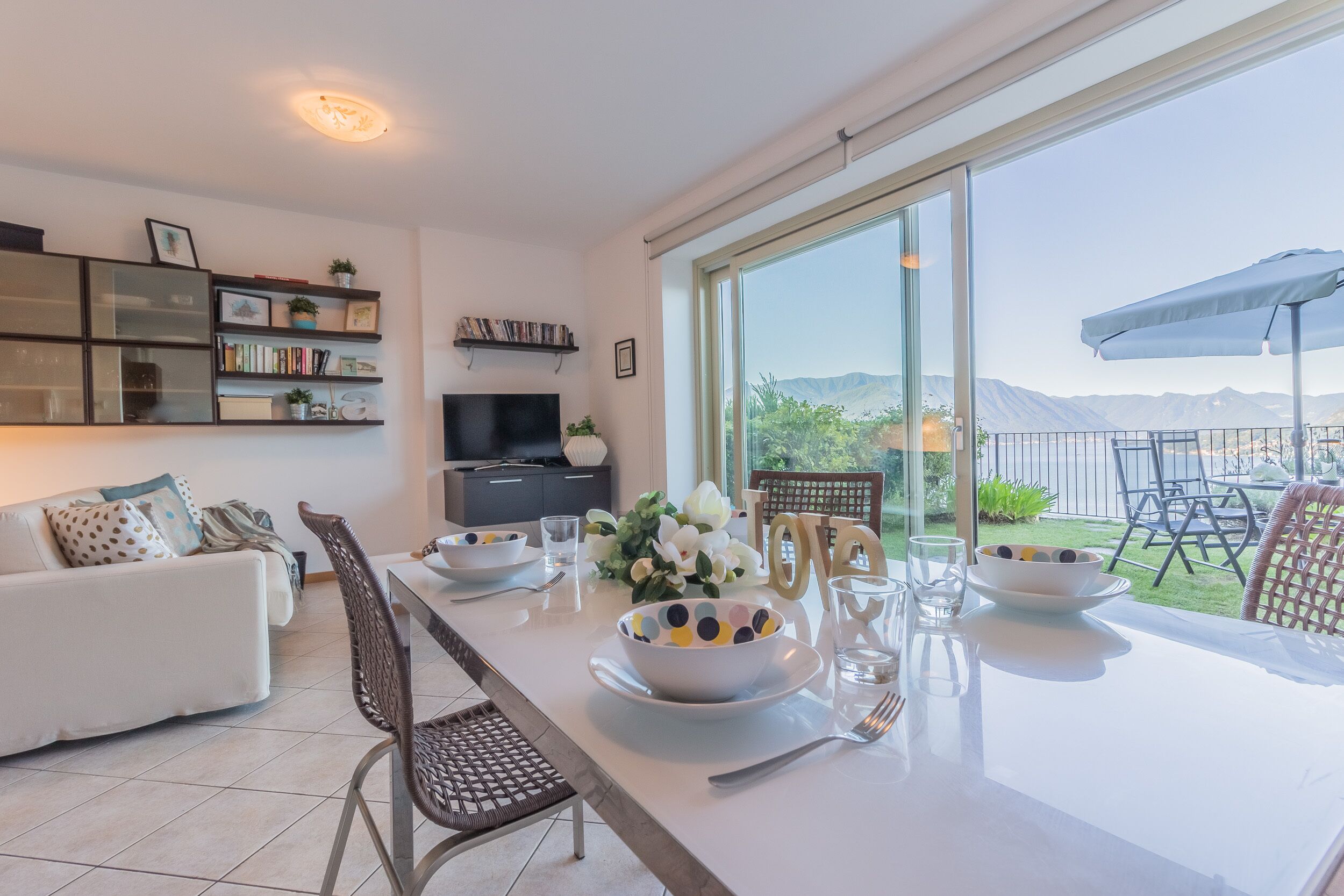 A modern living room with a dining area, large windows, and a view of mountains.