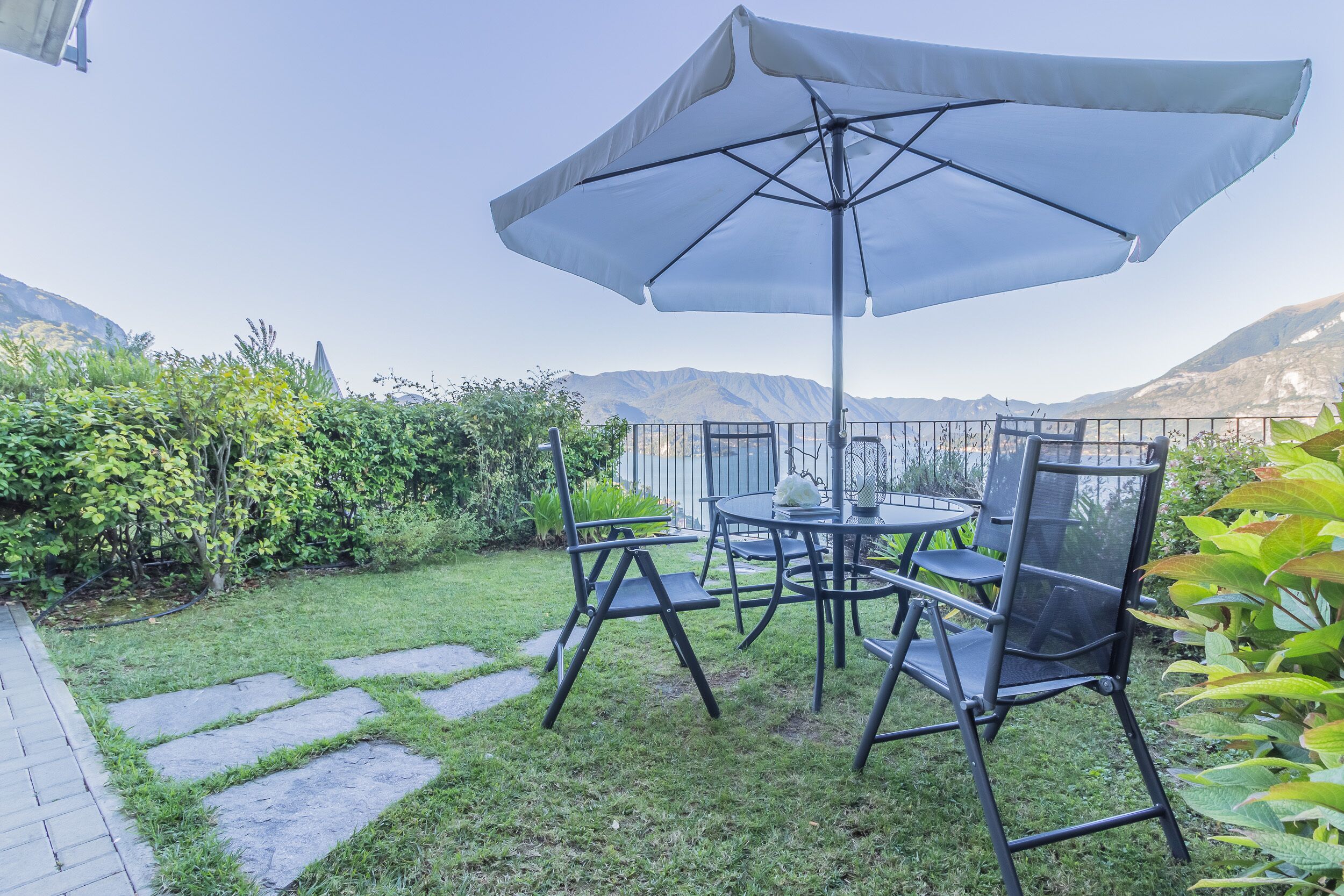 Terrassa exterior amb taula i cadires sota un parasol gran, envoltada de vegetació i vista a una muntanya.