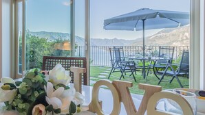 Una mesa con un ramo de flores blancas y letras de madera que deletrean 'love' en una habitación con ventanas grandes que dan a un patio con mobiliario exterior.