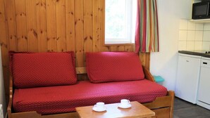 A cozy wooden sofa with red cushions, a small wooden table with two white cups, and a white kitchen area with a microwave. - Spacious 3-Room + Bunk Area, Sleeps 8, Close to Slopes and Shops in Vars Les Claux (Vars)