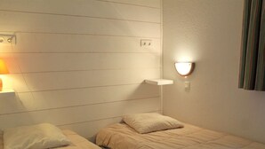 A small, single-bed room with a wooden panel wall, a bedside table with a lamp, and a wall-mounted light fixture. - Spacious 3-Room + Bunk Area, Sleeps 8, Close to Slopes and Shops in Vars Les Claux (Vars)