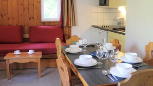A cozy room with a wooden sofa, a dining table set with plates, glasses, and cutlery, and a kitchen area with a microwave. - Spacious 3-Room + Bunk Area, Sleeps 8, Close to Slopes and Shops in Vars Les Claux (Vars)