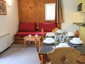 Um quarto acolhedor com um banco de madeira, uma mesa de jantar posta com pratos e copos, e uma cozinha com micro-ondas.