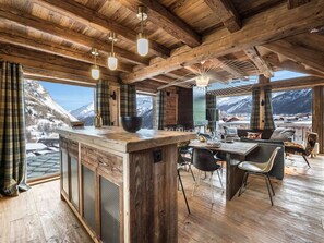 A rustic wooden interior with a bar area, dining space, and large windows offering mountain views. - Luxurious Chalet with Panoramic Views, Jacuzzi, Hammam, Near Slopes, Sleeps 10 (Val-d'Isère)