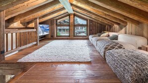 A cozy attic bedroom with wooden beams, a large window, a TV, and a sofa. - Luxurious Chalet with Panoramic Views, Jacuzzi, Hammam, Near Slopes, Sleeps 10 (Val-d'Isère)