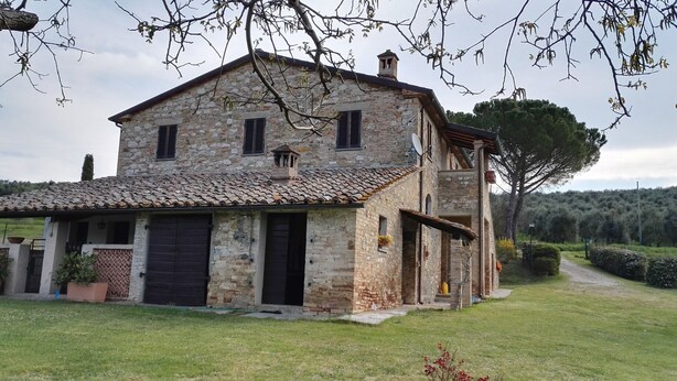 A stone farmhouse with a tiled roof, a large front door, and a small porch. - Podere Collesanto (Umbria)