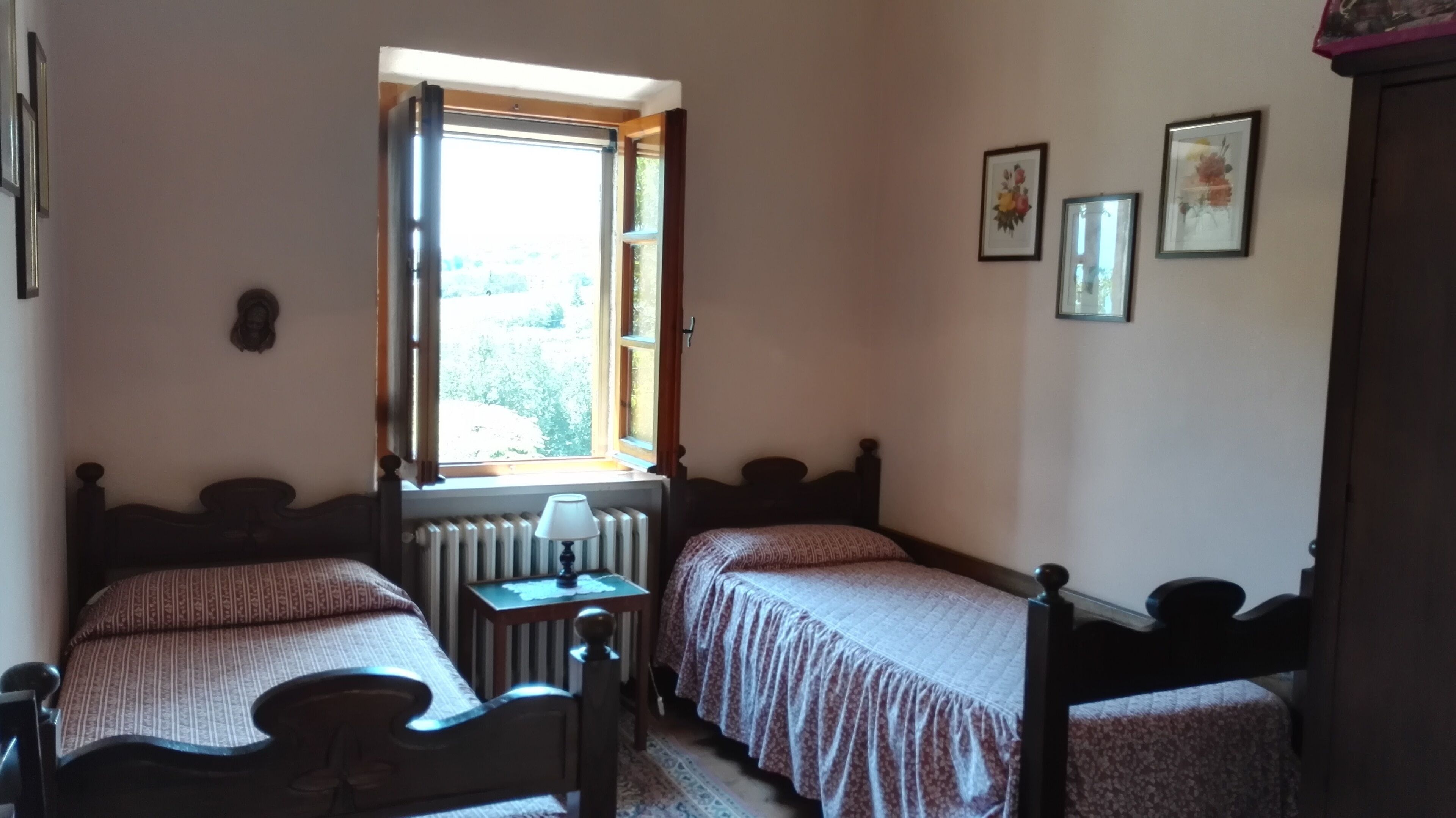 A bedroom with two single beds, a radiator, a window, and a small table.