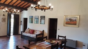 A dining area with a wooden table, chairs, a sofa with floral cushions, and a chandelier. - Podere Collesanto (Umbria)