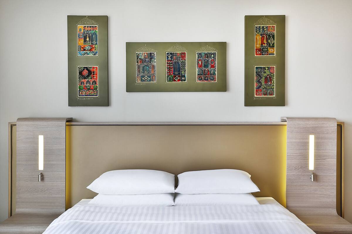 A modern hotel room with a bed, two bedside tables, and a wall-mounted artwork.