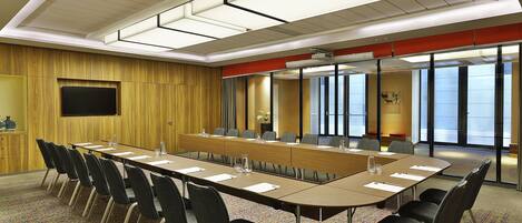 A conference room with a long table, chairs, a TV, and a large window.