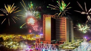A cityscape at night with fireworks in the sky and a prominent building with a grid-like facade.