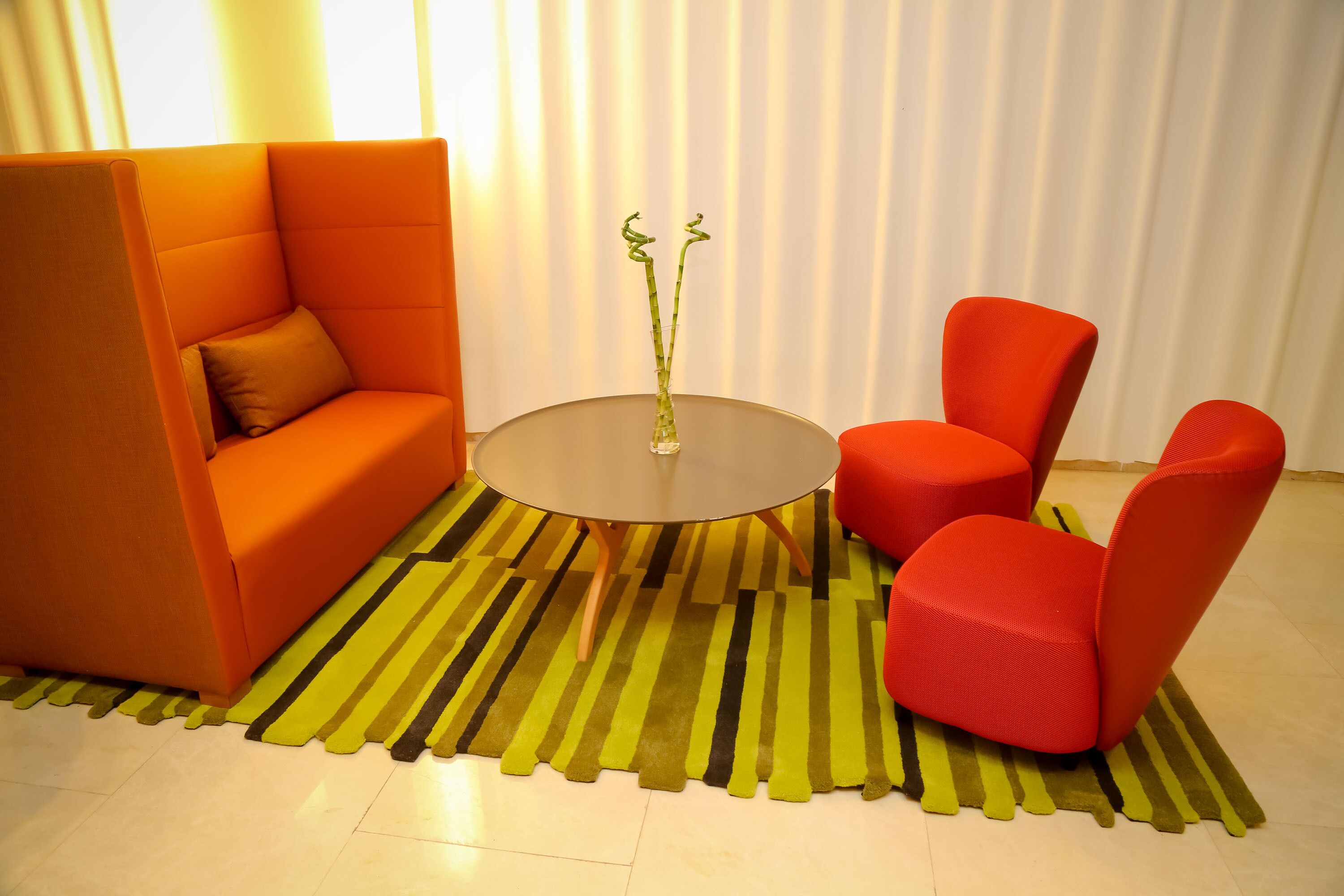 Un salón moderno con un sofá, dos sillones rojos, una mesa redonda y una alfombra a rayas.