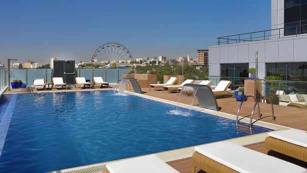 A rooftop pool with lounge chairs, a water feature, and a Ferris wheel in the background.