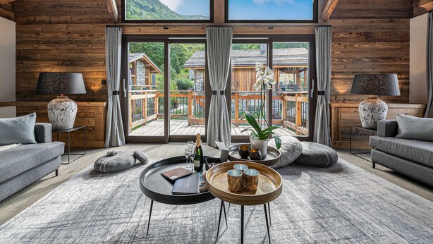 A spacious room with a high ceiling, wooden beams, large windows, and a view of a mountain. There are two sofas, a coffee table, and a side table with lamps. - Authentic chalet with sauna and shuttle in Saint Martin (Saint-Martin-de-Belleville)
