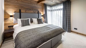 A bedroom with a wooden ceiling, a bed with a grey and white duvet, and a nightstand with a lamp. - Authentic chalet with sauna and shuttle in Saint Martin (Saint-Martin-de-Belleville)