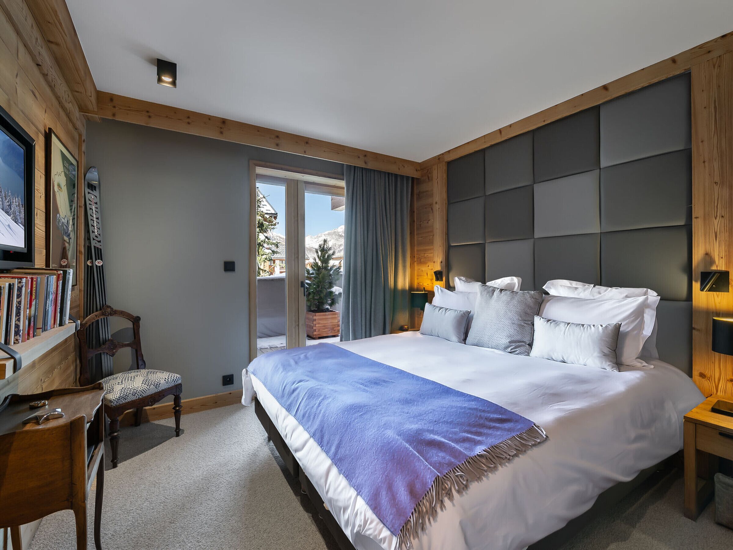 A modern hotel room with a large bed, a wooden headboard, a desk with a chair, and a television on the wall.
