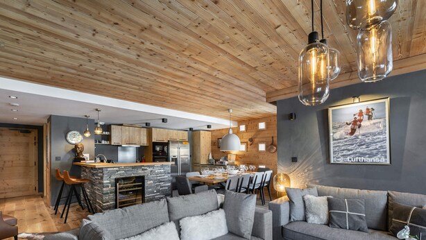 A modern living room with a grey sofa, a dining area with a wooden table, and a kitchen with a stone island. - Contemporary 4-Bedroom Apartment Near Ski Slopes with Fireplace and Parking (Val-d'Isère)