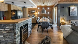 A modern kitchen with wooden cabinets and a stone island, a dining area with a large table and chairs, and a cozy living area with a sofa and a lamp. - Contemporary 4-Bedroom Apartment Near Ski Slopes with Fireplace and Parking (Val-d'Isère)