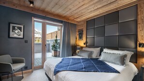 A modern bedroom with a large bed, a wooden ceiling, a sliding glass door to a balcony, and a framed picture on the wall. - Contemporary 4-Bedroom Apartment Near Ski Slopes with Fireplace and Parking (Val-d'Isère)