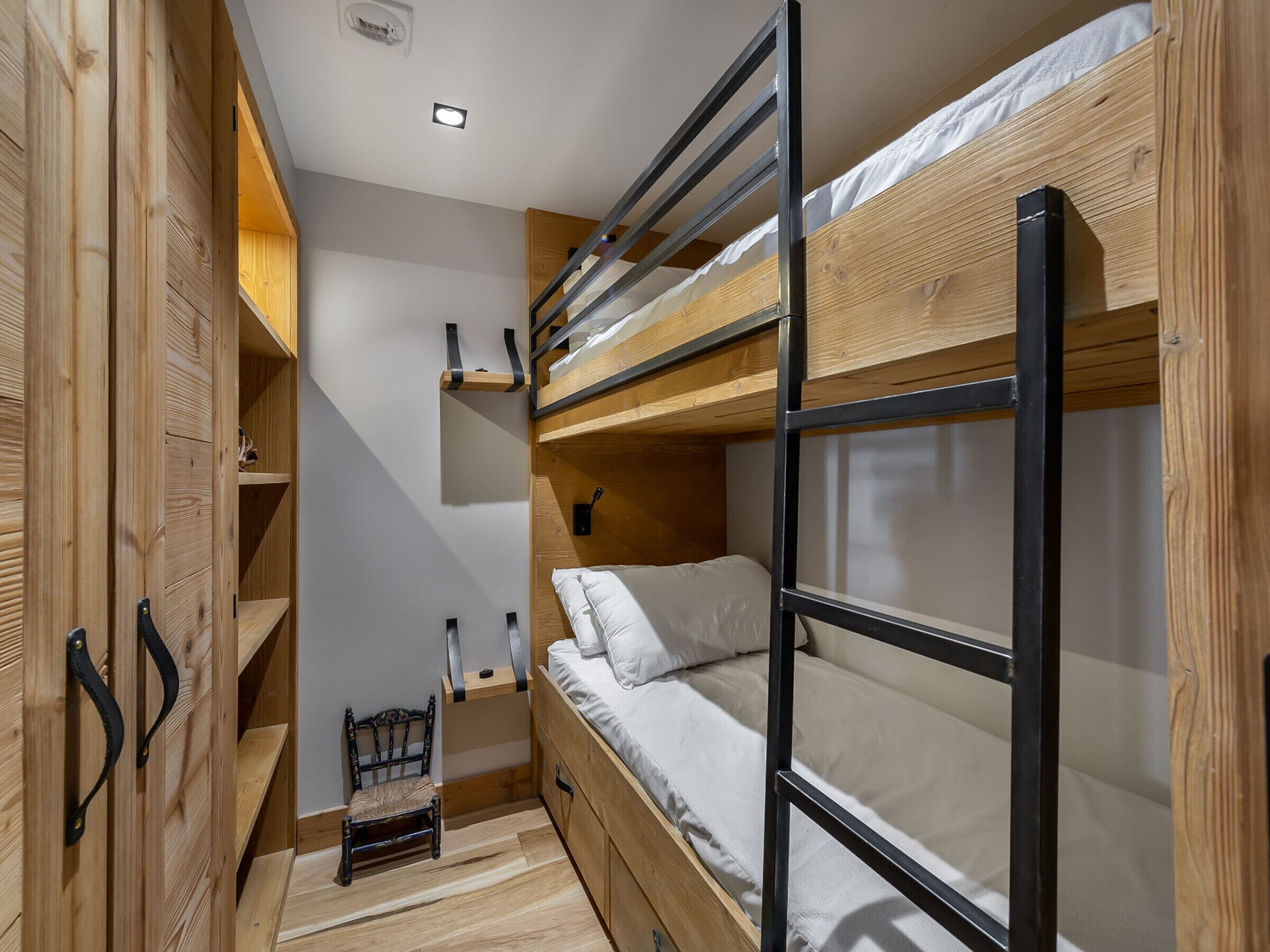 A bunk bed room with wooden walls and a small chair.
