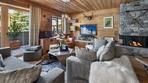 A cozy living room with a stone fireplace, wooden ceiling, and a television. - Contemporary 4-Bedroom Apartment Near Ski Slopes with Fireplace and Parking (Val-d'Isère)