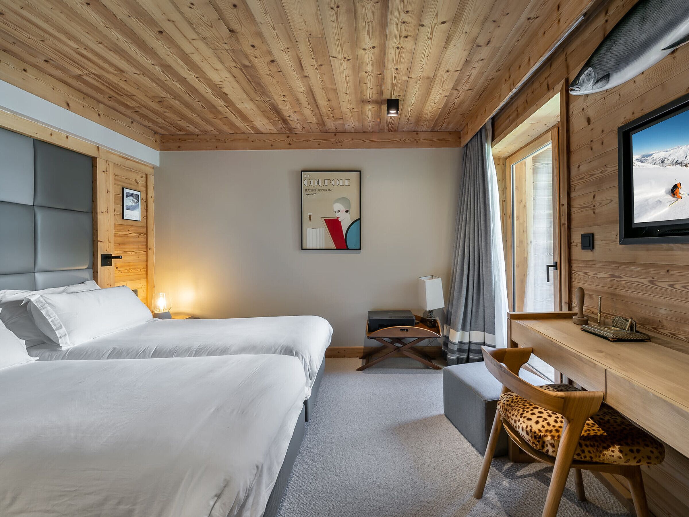 Une chambre d’hôtel avec deux lits, un bureau avec une chaise, une télévision et une fenêtre donnant sur un paysage enneigé.