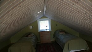 Une petite chambre mansardée avec deux lits, une fenêtre et une commode.