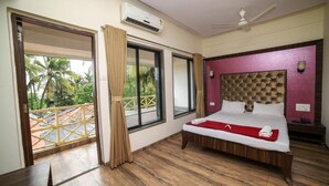 A hotel room with a bed, a ceiling fan, an air conditioning unit, and a balcony with a view of palm trees. - Seashell Beach Resort (Dahanu)