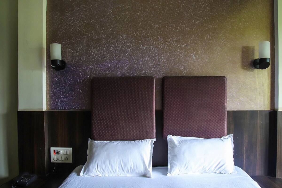 A hotel room with a large bed, two pillows, a nightstand, a phone, and a wall-mounted light fixture.