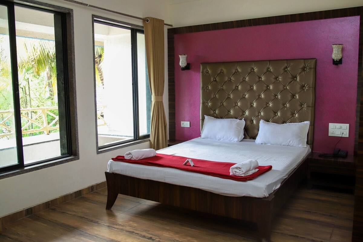 A hotel room with a large bed, a wooden floor, and a view of palm trees through the windows.