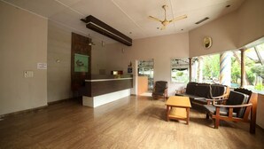 A reception area with a wooden reception desk, a sofa, and a table. - Seashell Beach Resort (Dahanu)