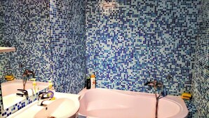 A bathroom with a pink bathtub, two sinks, and mosaic tile walls.