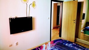 A room with a bed, a mounted television, and a door leading to another room.