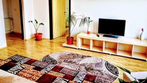 A living room with a flat-screen TV on a white stand, a patterned rug, and potted plants.