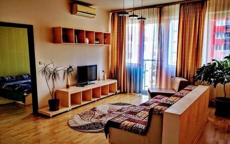 A living room with a sofa, TV, shelves, and a potted plant.