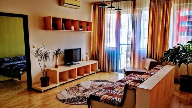 A living room with a sofa, TV, shelves, and a potted plant.