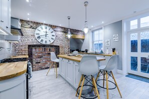 A modern kitchen with a brick wall, a large clock, and a bar area. - Augustus House (Chester)