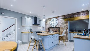 A modern kitchen with a central island, white cabinetry, and a brick accent wall. - Augustus House (Chester)