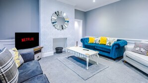 A modern living room with a blue sofa, a white armchair, a coffee table, and a fireplace. - Augustus House (Chester)