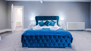 A bedroom with a large bed, two bedside tables with lamps, a radiator, and a door leading to another room. - Augustus House (Chester)