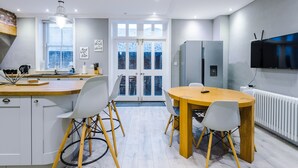 A modern kitchen with a central island, white cabinetry, and a dining area with a round table and chairs. - Augustus House (Chester)