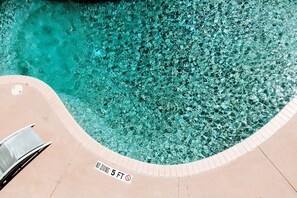 Una piscina azul cristalina con un letrero que dice 'NO DIVING 5 FT', una tumbona y un solárium con baldosas.