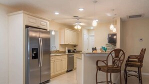 A kitchen with a stainless steel refrigerator, wooden cabinets, a dishwasher, and a bar area with two wooden chairs. - 4 Bed 2 Bath near Siesta Key - Pet Friendly (Sarasota)
