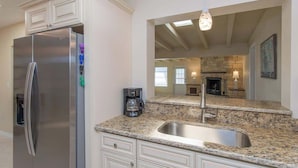 A kitchen with a stainless steel refrigerator, granite countertops, a built-in sink, and a stone fireplace in the background. - 4 Bed 2 Bath near Siesta Key - Pet Friendly (Sarasota)