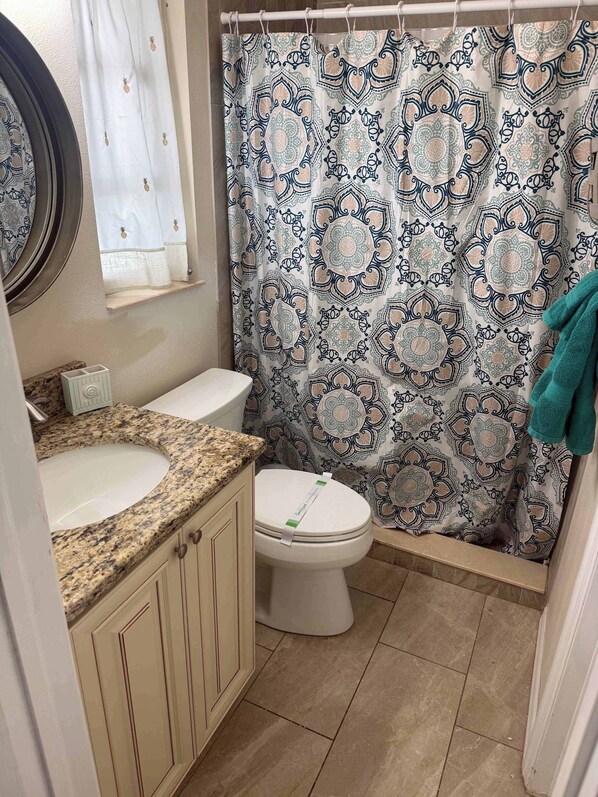 A bathroom with a patterned shower curtain, a sink with a granite countertop, and a toilet. - 4 Bed 2 Bath near Siesta Key - Pet Friendly (Sarasota)