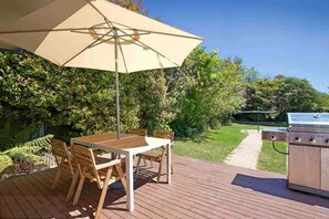 An outdoor deck with a wooden table and chairs, a large umbrella, and a grill.